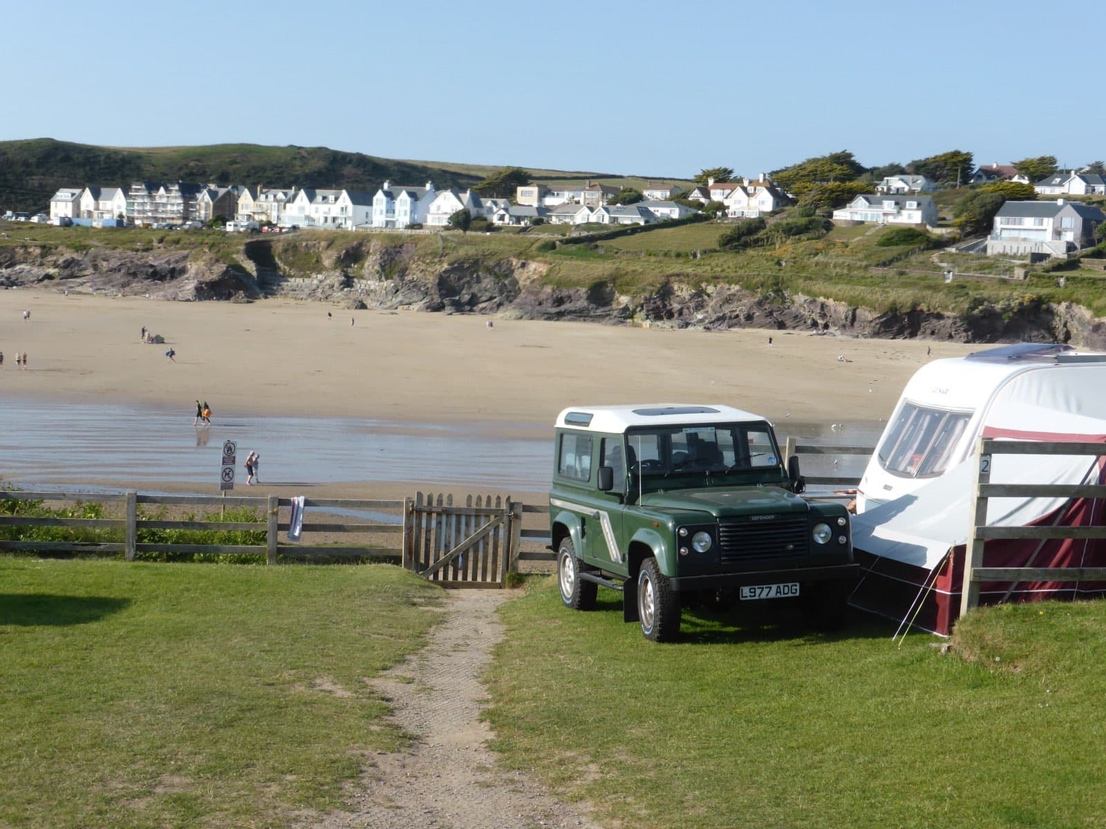 A green Defender 90 County towing a caravan beside a beach in Cornwall