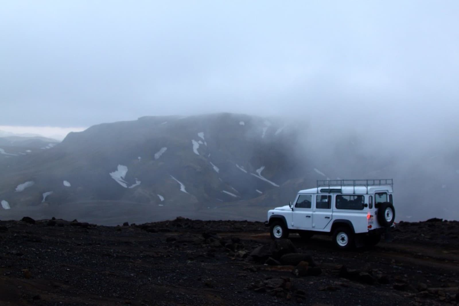 A white Defender 110 parked alone in the fog of the Icelandic highlands