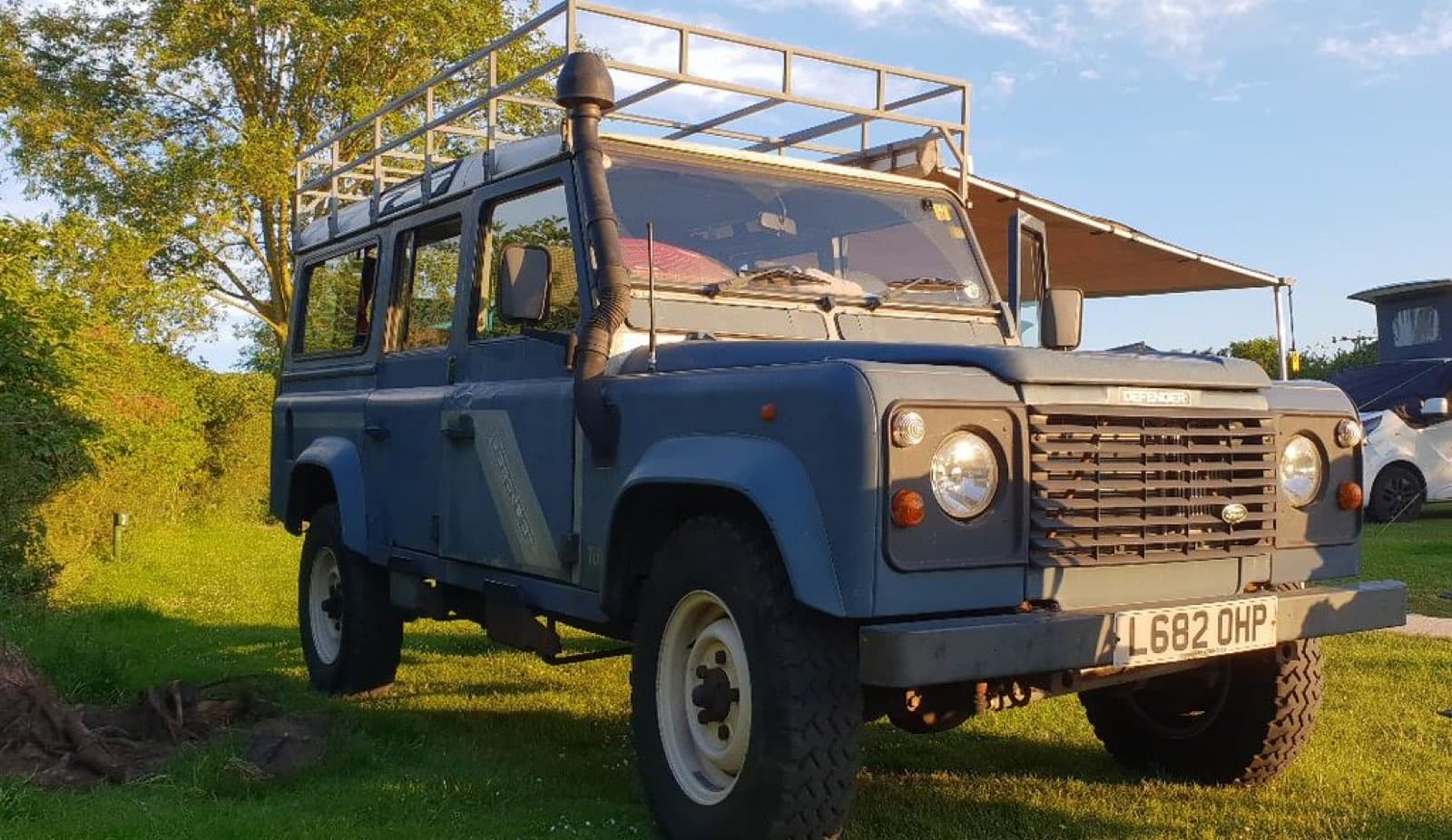 A well-used Defender 110 in evening light with its awning out on holiday